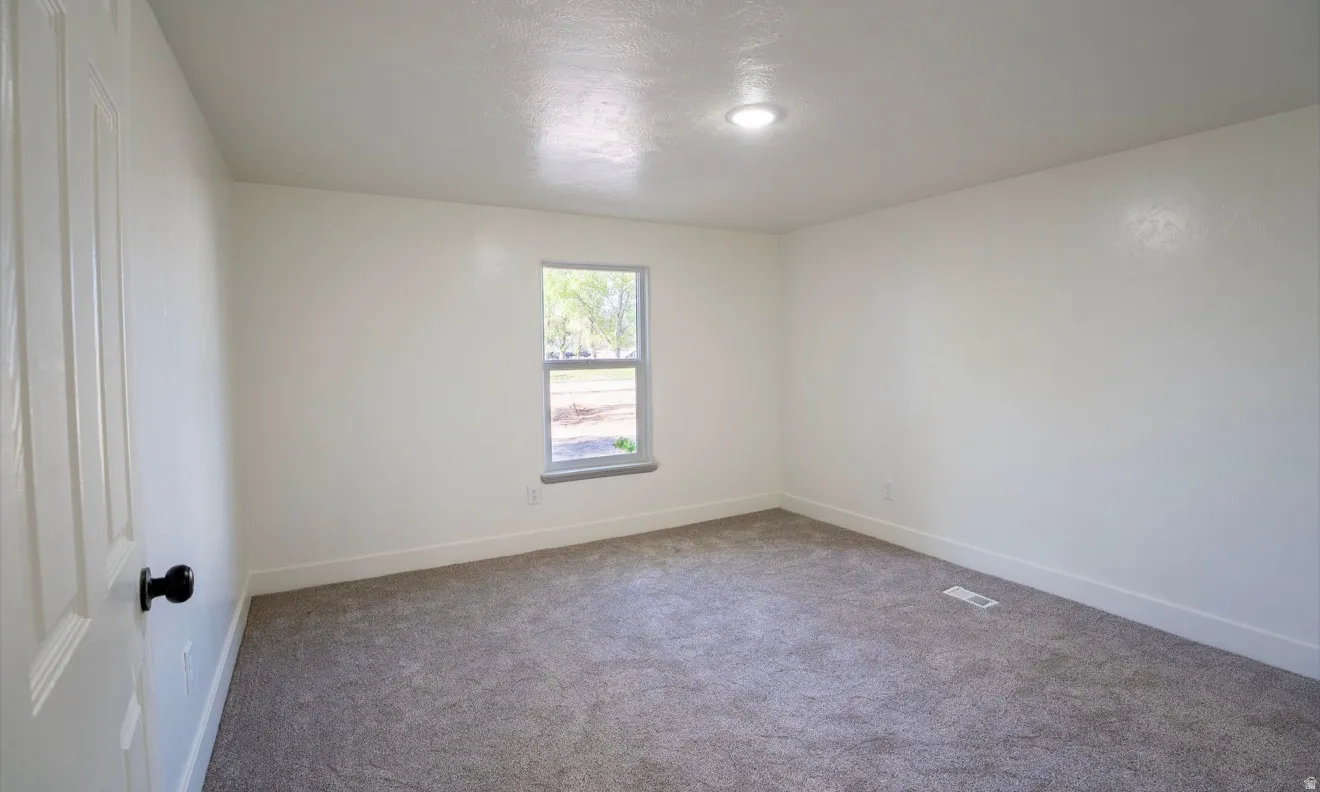 Carpeted room featuring a single window with white trim, a flush-mount ceiling light, white walls, and white baseboards