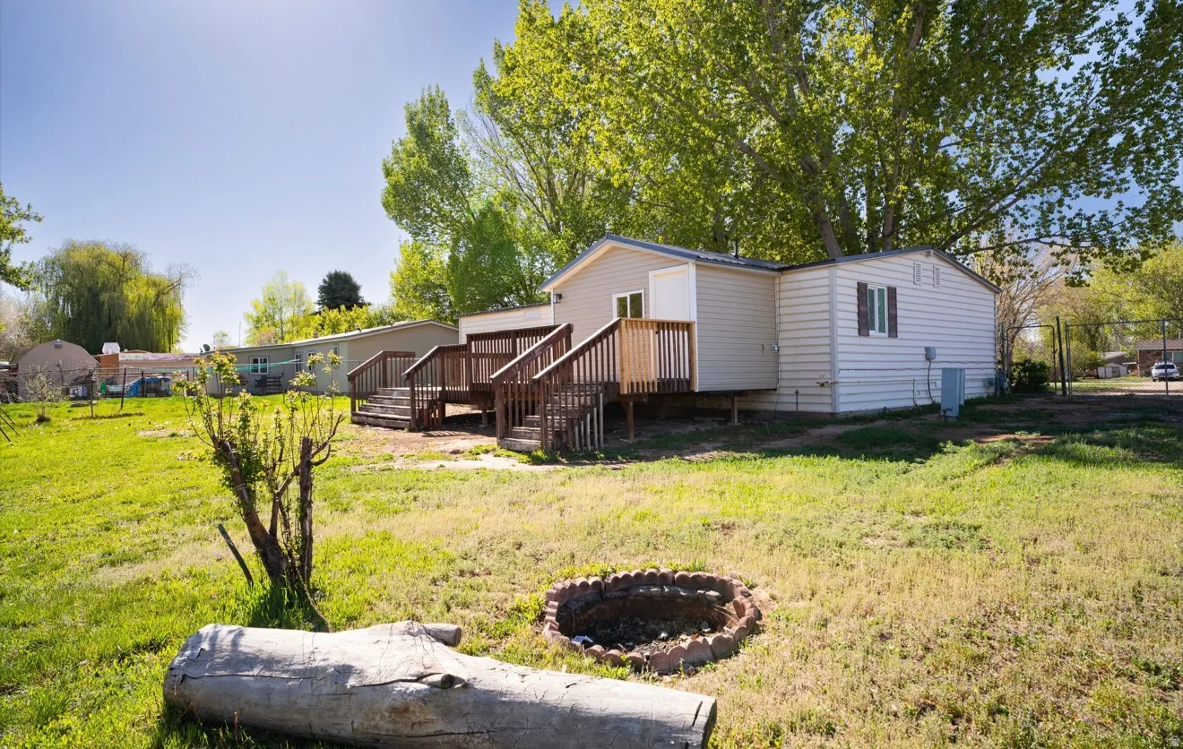 Rear exterior featuring a spacious wood deck with railings, dual staircases, and a stone-lined fire pit