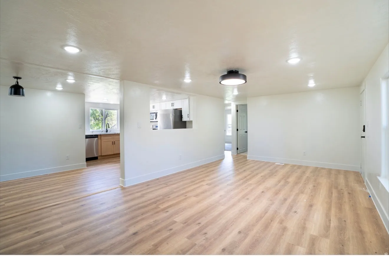 Spacious living area featuring light wood-finish flooring, recessed lighting, a modern flush-mount ceiling fixture, and a pass-through opening to the kitchen area