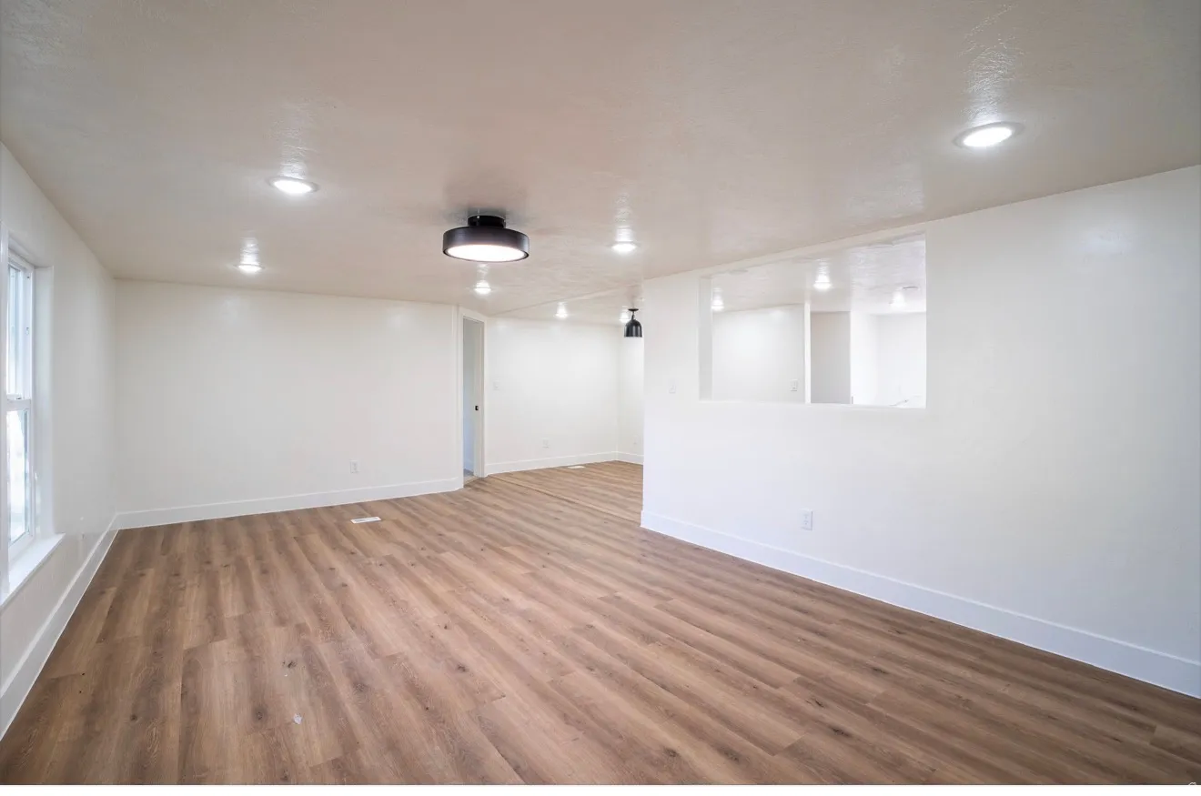 Spacious room featuring wood-finish flooring, recessed lighting, a modern ceiling fixture, and a pass-through window