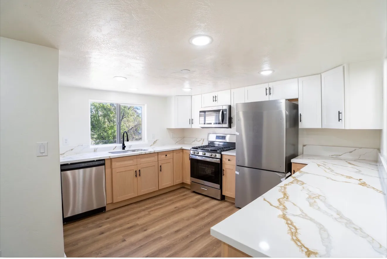 Modern kitchen featuring white upper cabinetry, wood-finish lower cabinetry, wood-finish flooring, recessed lighting, and stainless steel appliances