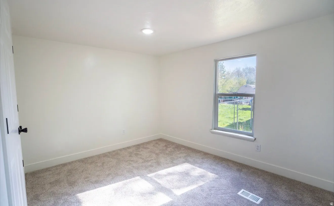 Bright room featuring neutral wall tones, plush gray carpeting, a single window, recessed lighting, and white baseboards
