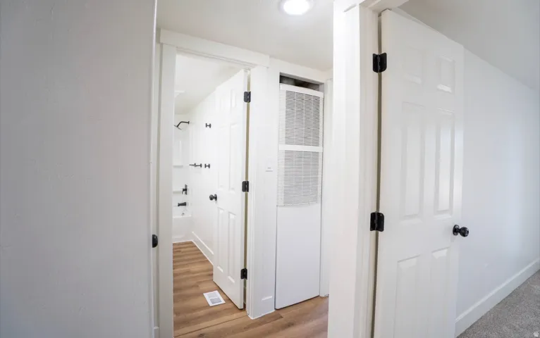 White paneled interior doors with black hardware, wood-finish flooring, recessed lighting, and a white bathtub with black fixtures