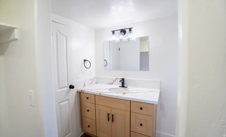 Bathroom vanity featuring a light wood-finish cabinet with black hardware, a white countertop with subtle veining, an undermount sink, and a matte black faucet