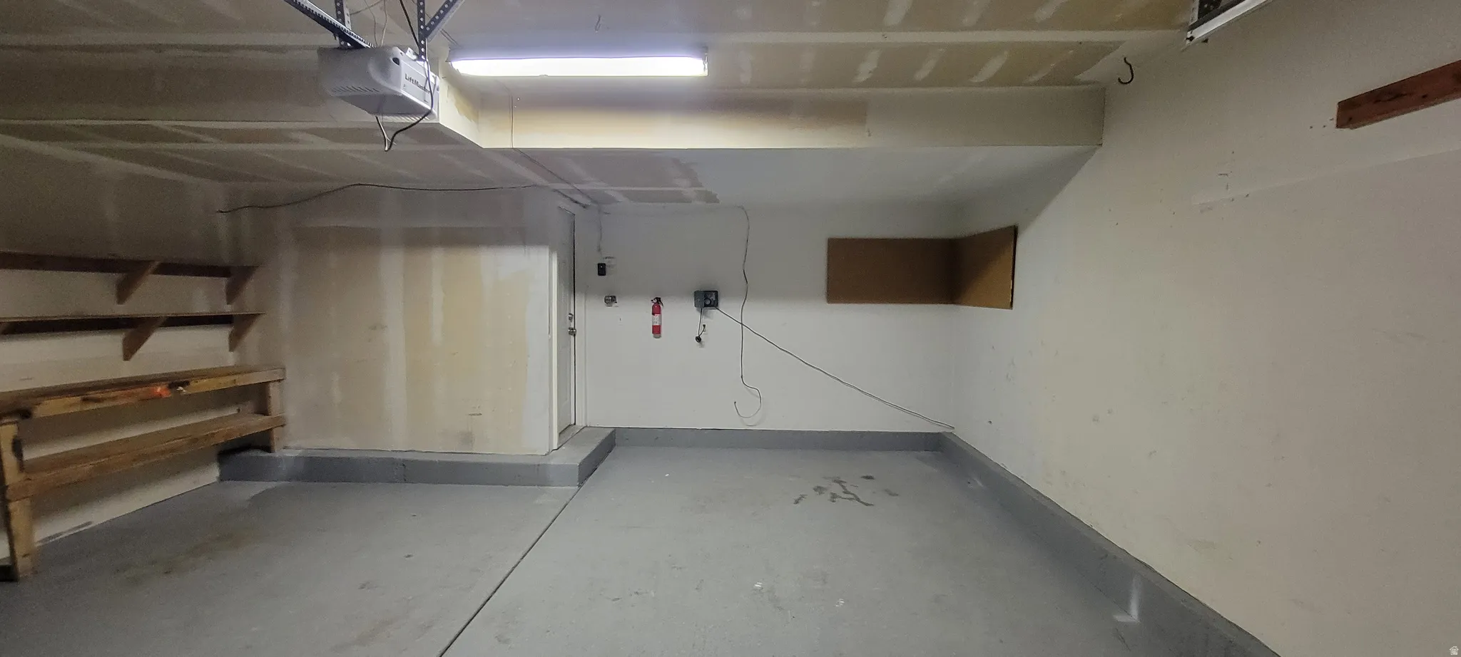 Garage interior featuring a light-colored floor, built-in shelving, overhead lighting, and an automatic garage door opener mechanism