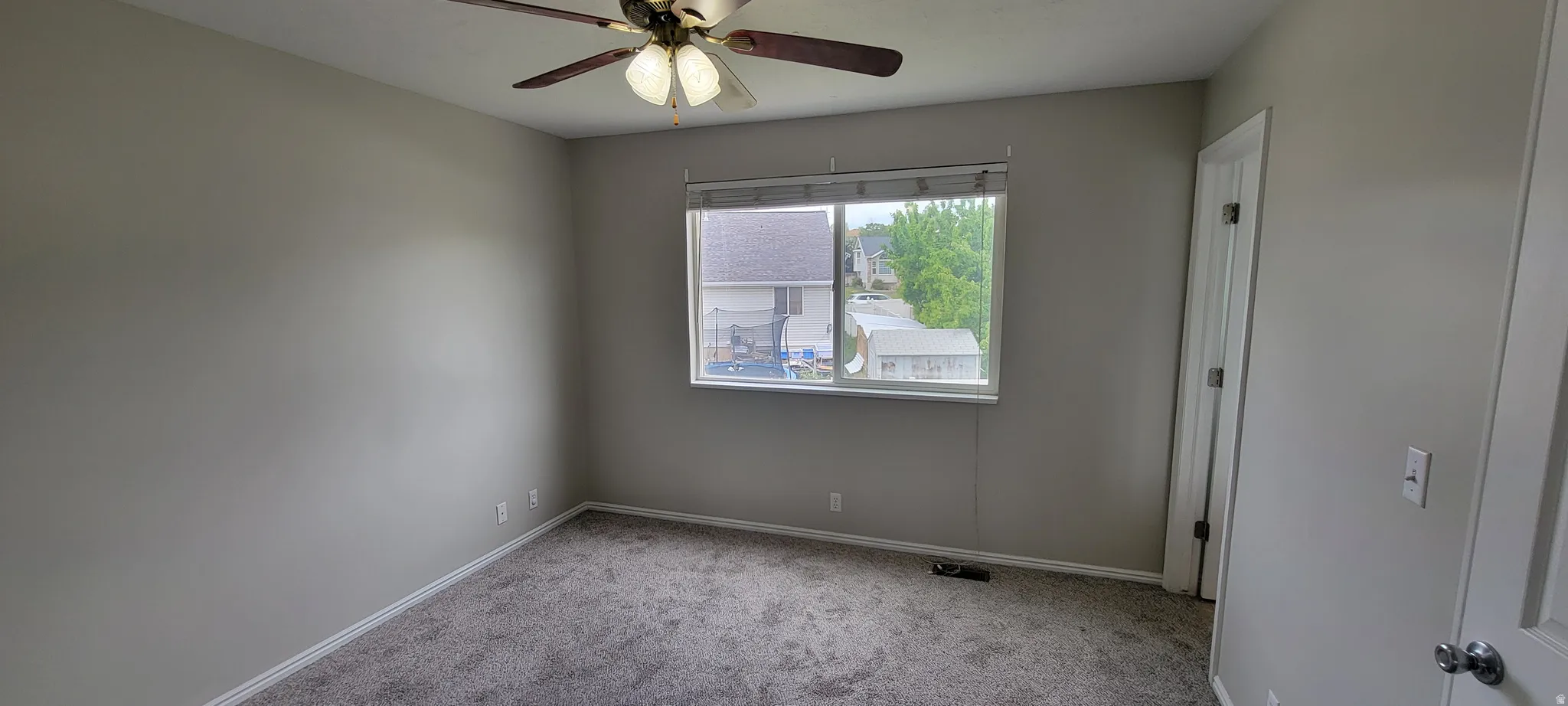 Carpeted room featuring a ceiling fan with light fixture, a window with horizontal blinds, and neutral wall tones