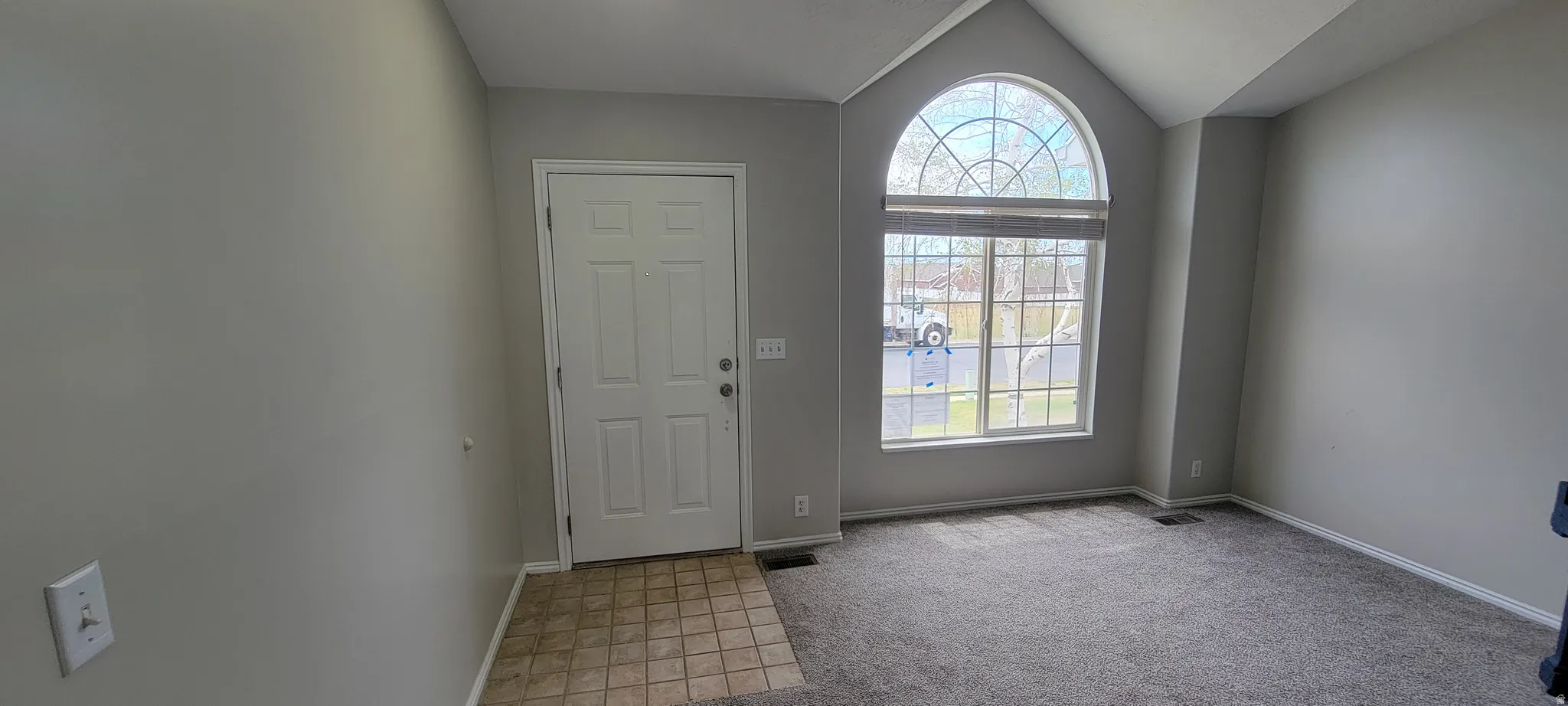 Entryway featuring a decorative arched window, vaulted ceilings, and a paneled entry door