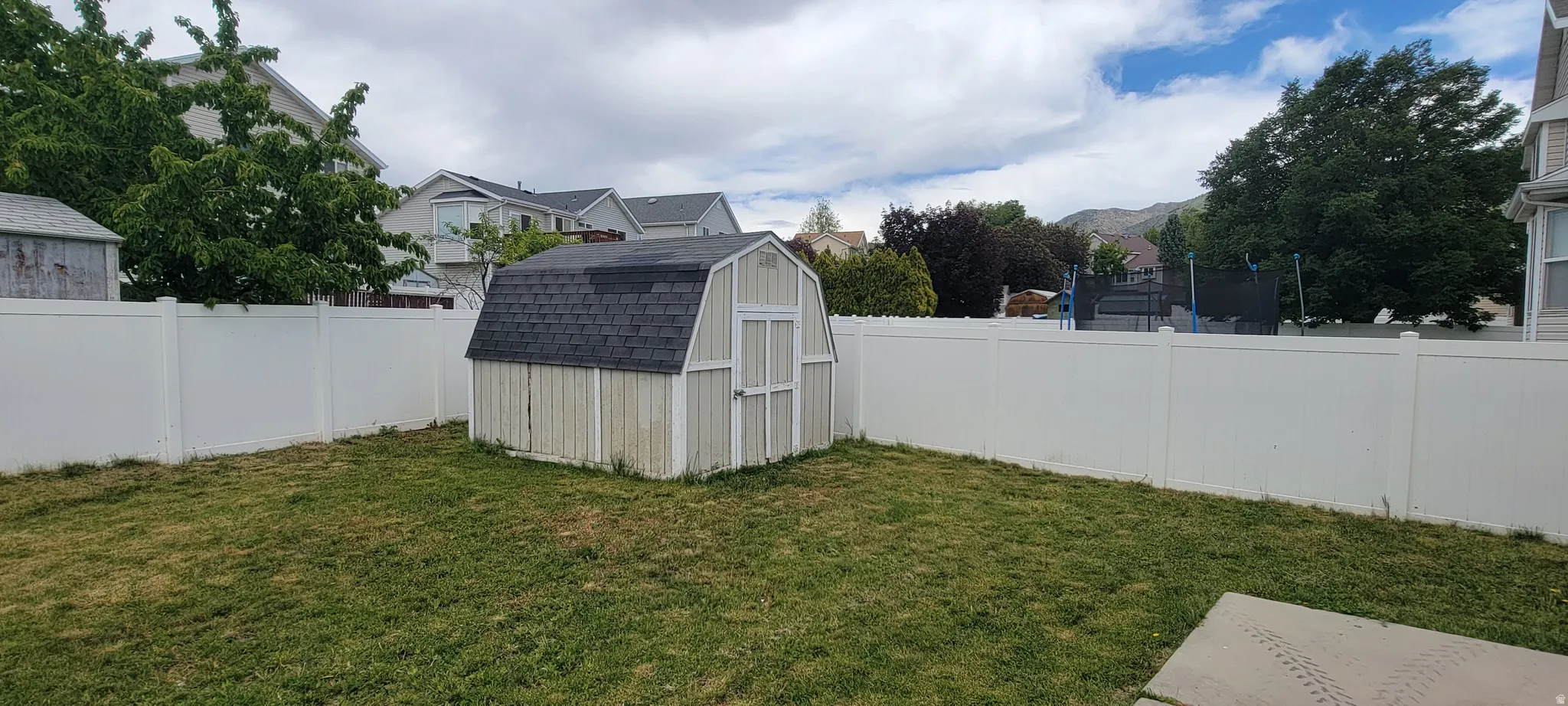 Expansive backyard featuring a white vinyl privacy fence, a storage shed with a gambrel roof, and a concrete pad