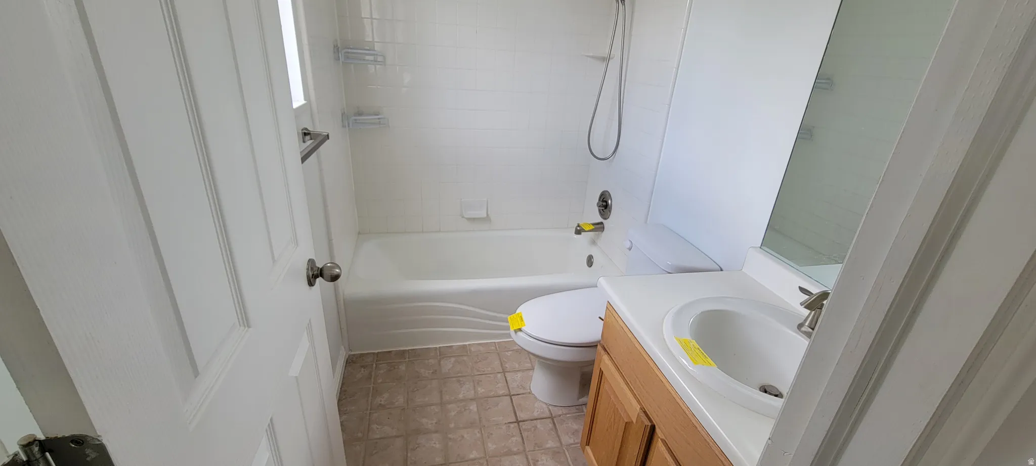 Full bathroom featuring a white tub/shower combination with a tiled surround, a white toilet, and a vanity with a white countertop and natural wood-finish cabinetry