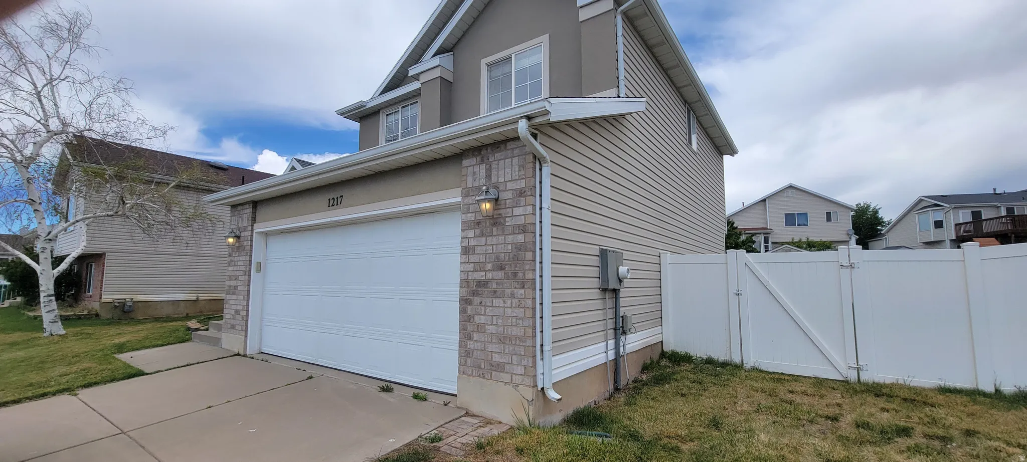 Two-story residence featuring a two-car garage with overhead door, a brick veneer facade accent, and light-colored siding
