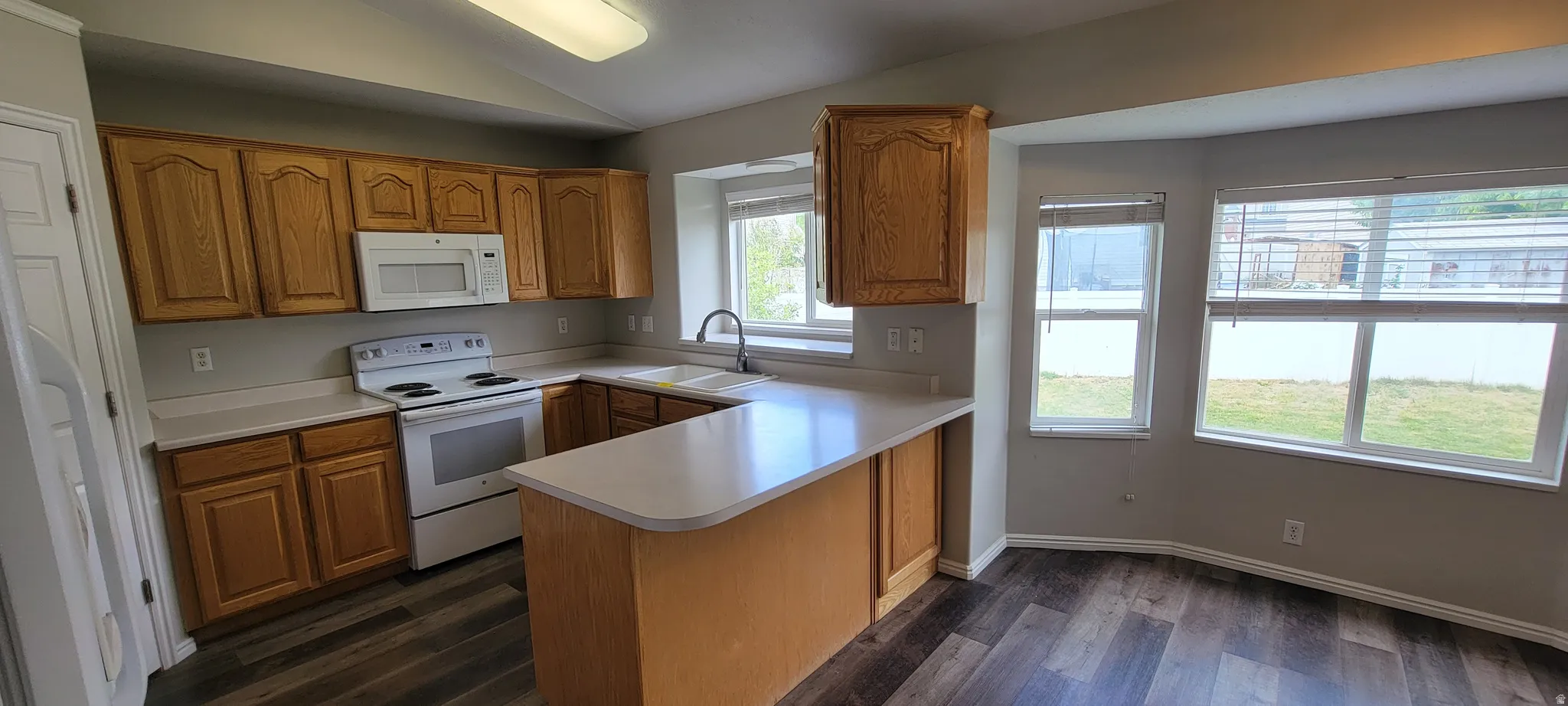 Kitchen featuring wood-finish cabinetry, white appliances, a peninsula with countertop seating, a double basin sink, and wood-finish flooring