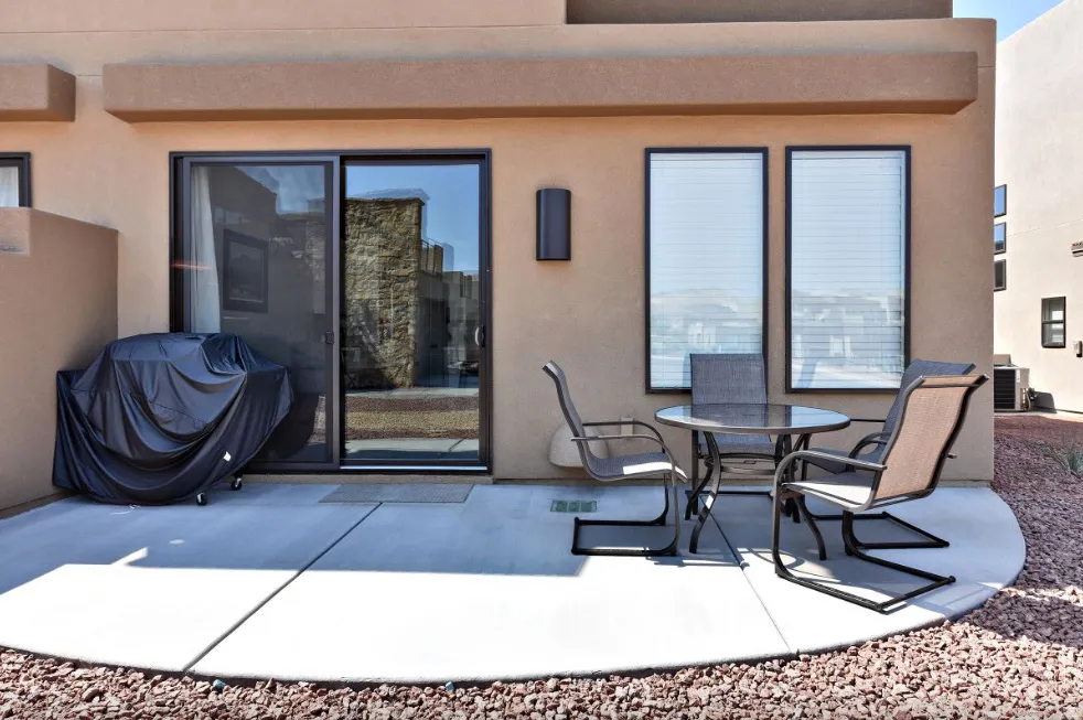 Private patio space featuring a sliding glass door, two large windows, an exterior wall sconce, and surrounding decorative gravel