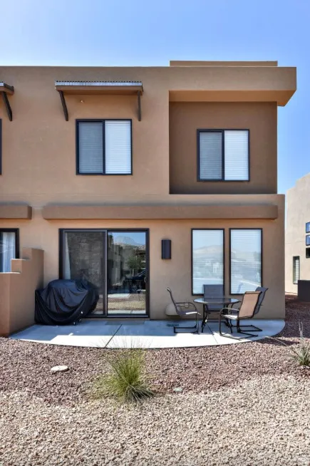 Contemporary stucco exterior featuring a curved concrete patio, sliding glass door, and upper-level windows with exterior shades