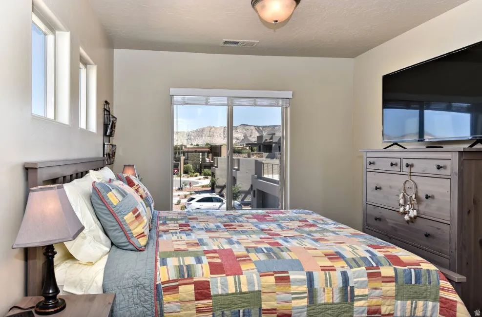 Bedroom featuring a full-light sliding glass door, a wall-mounted flat-screen display, and an adjacent window bank