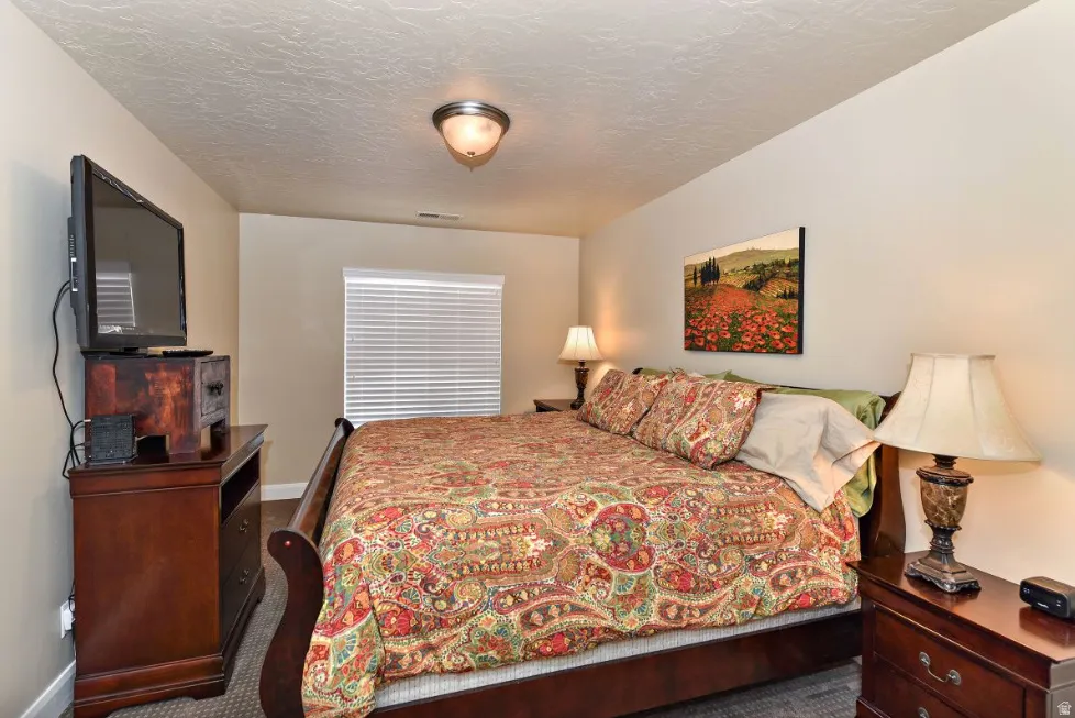 Carpeted bedroom featuring a window with blinds, a ceiling-mounted light fixture, and neutral wall tones