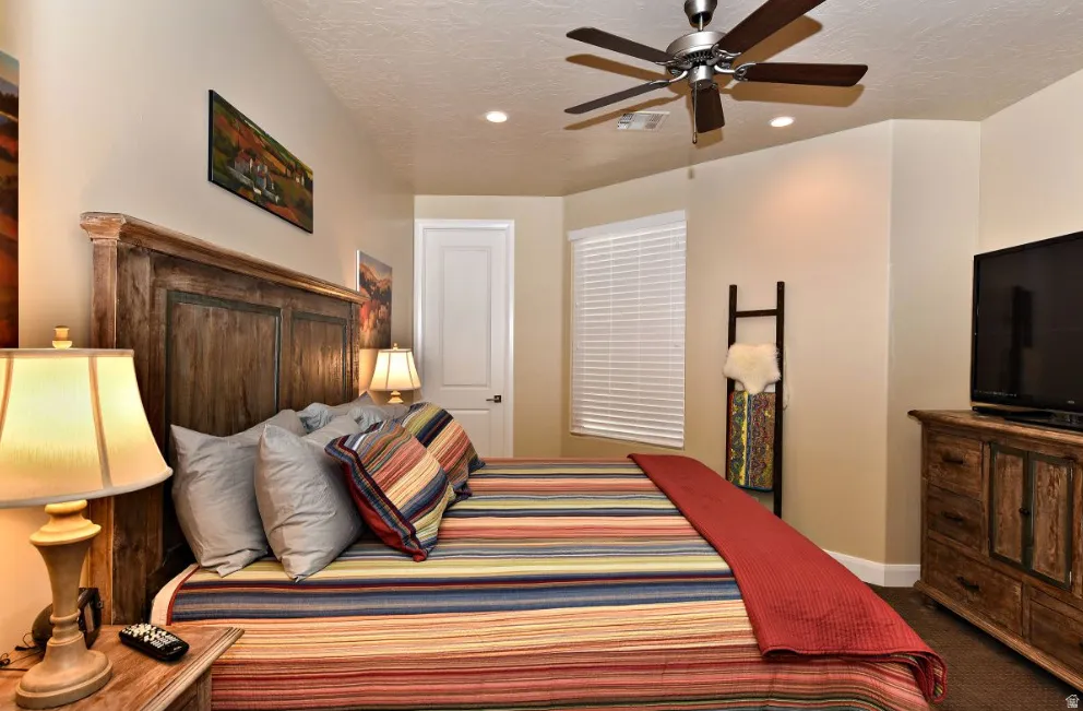 Interior room featuring a wood-finish headboard, textured beige walls, and a ceiling fan with integrated lighting