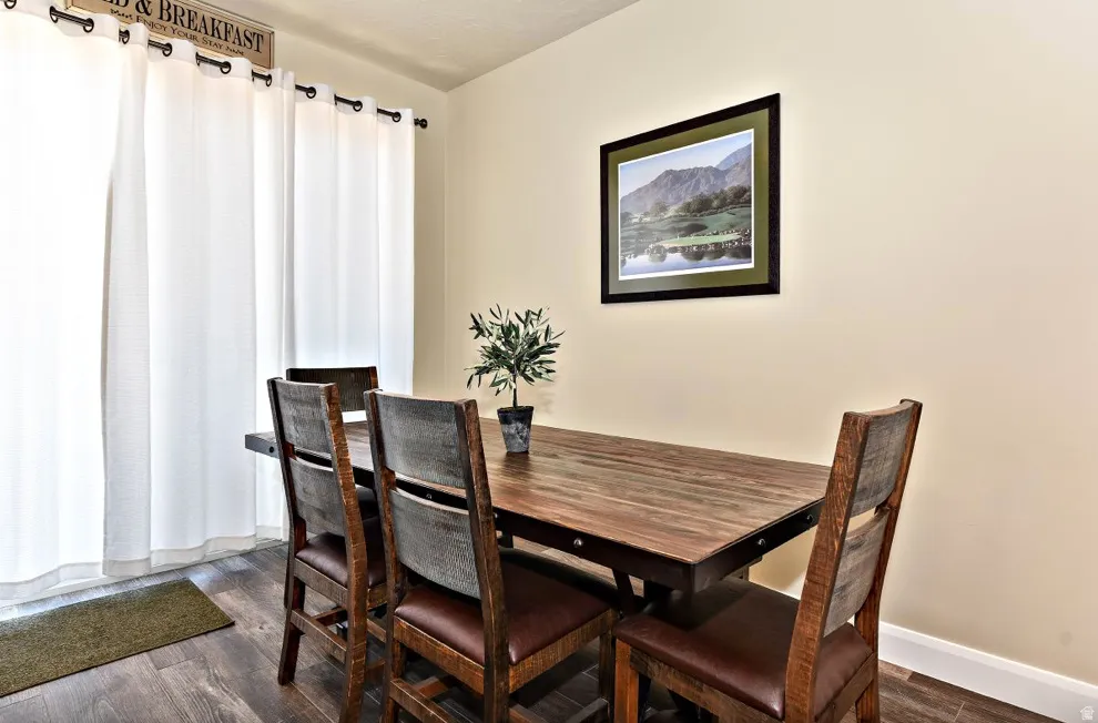 Dining space featuring wood-finish flooring, light-toned walls, and a large window with white curtains