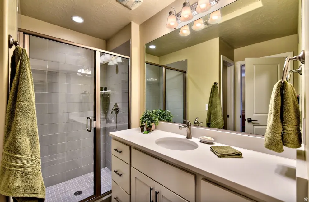 Spacious bathroom featuring a glass-enclosed shower with subway tile surround, a large vanity with an integrated sink, and a wall-mounted mirror with overhead lighting