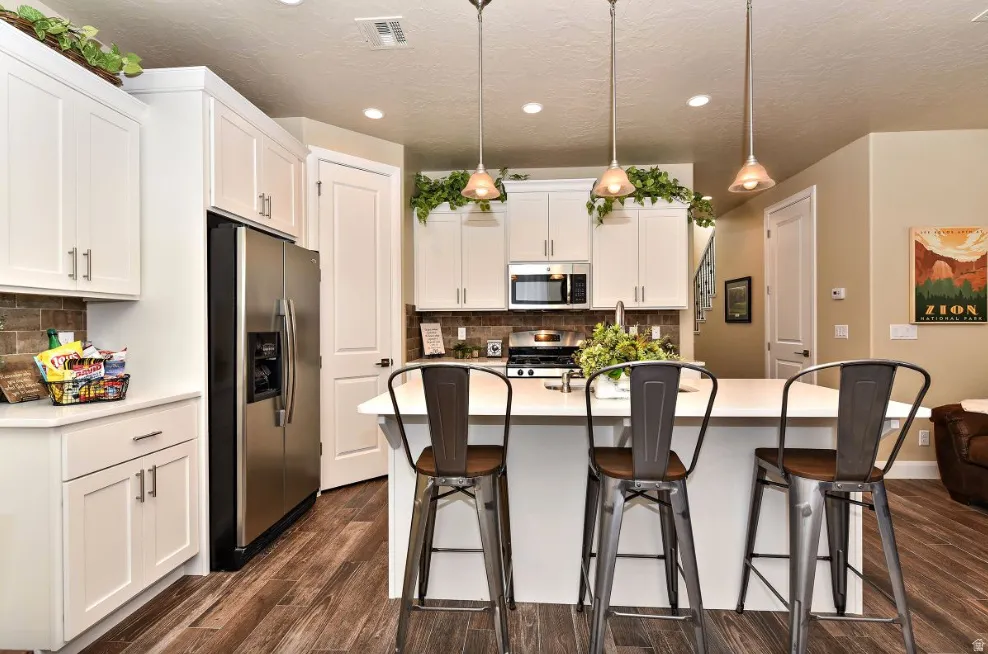 Kitchen featuring white cabinetry, stainless steel appliances, wood-finish flooring, a central island with bar seating, and pendant lighting