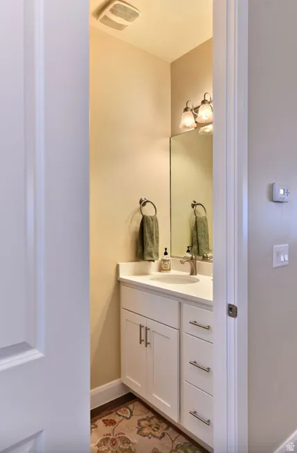 Powder room featuring a white vanity with brushed nickel hardware, a white countertop with an undermount sink, a wall-mounted mirror, and a two-light vanity fixture