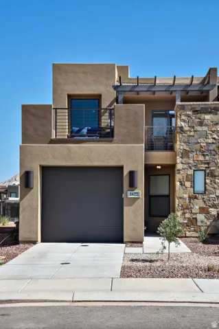 Stucco exterior with stone accent facade, featuring a dark tone garage door, an upper balcony with metal railing, and a second-story patio with pergola