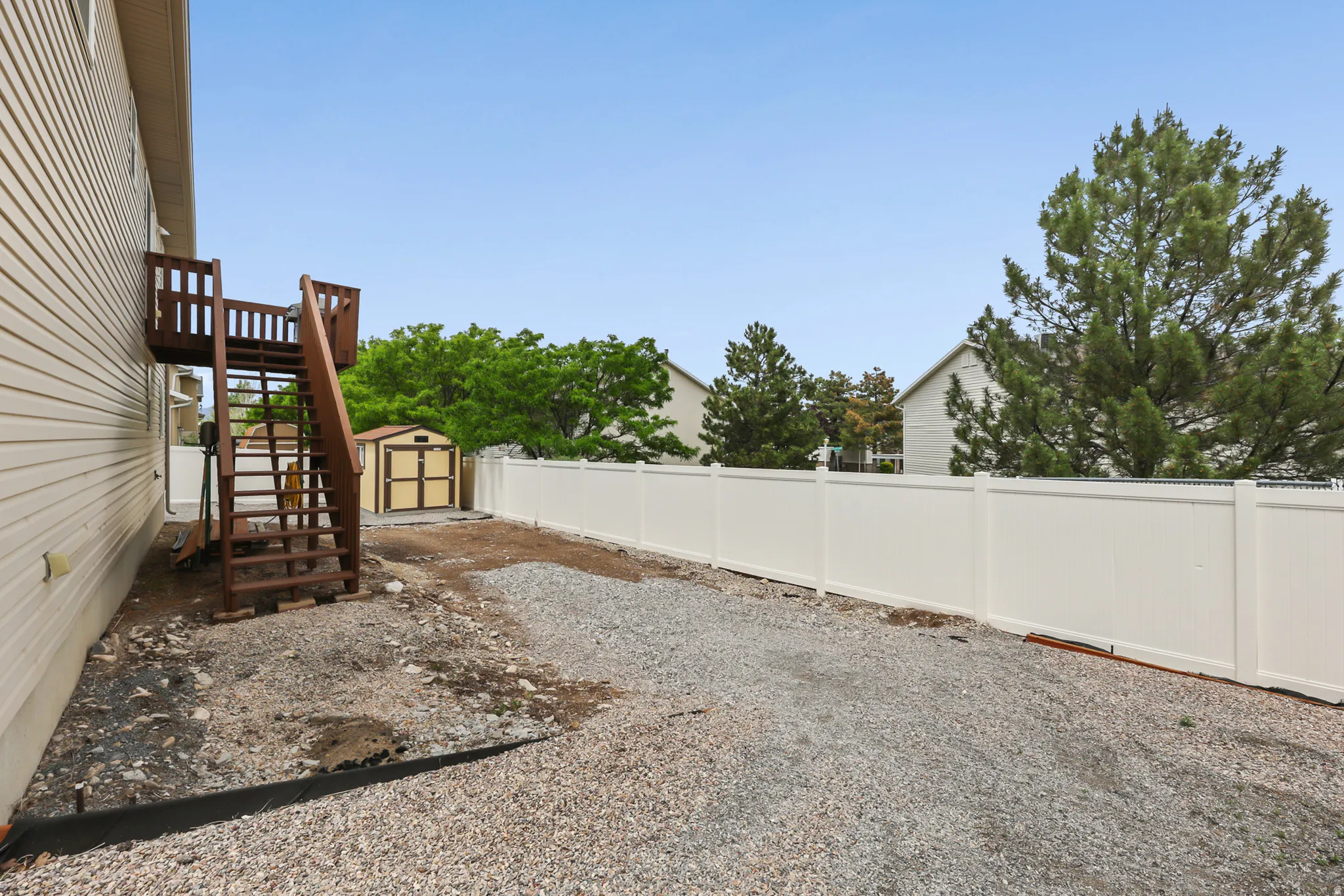 Side yard featuring a gravel surface, a multi-level deck with stairs, a shed, and a white privacy fence