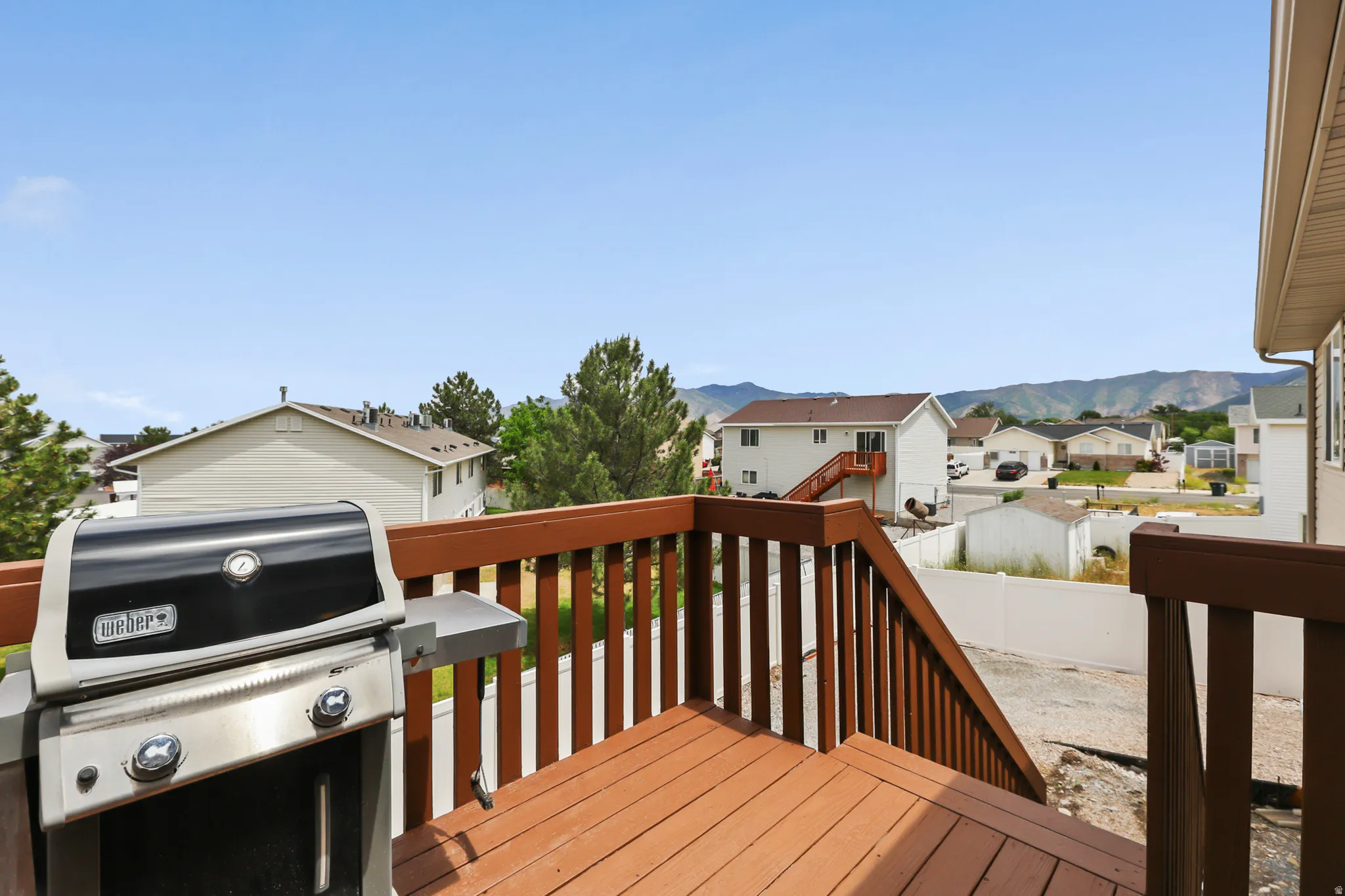 Expansive wood-finish deck with integrated railing and stairs, offering broad neighborhood scenery and distant mountains