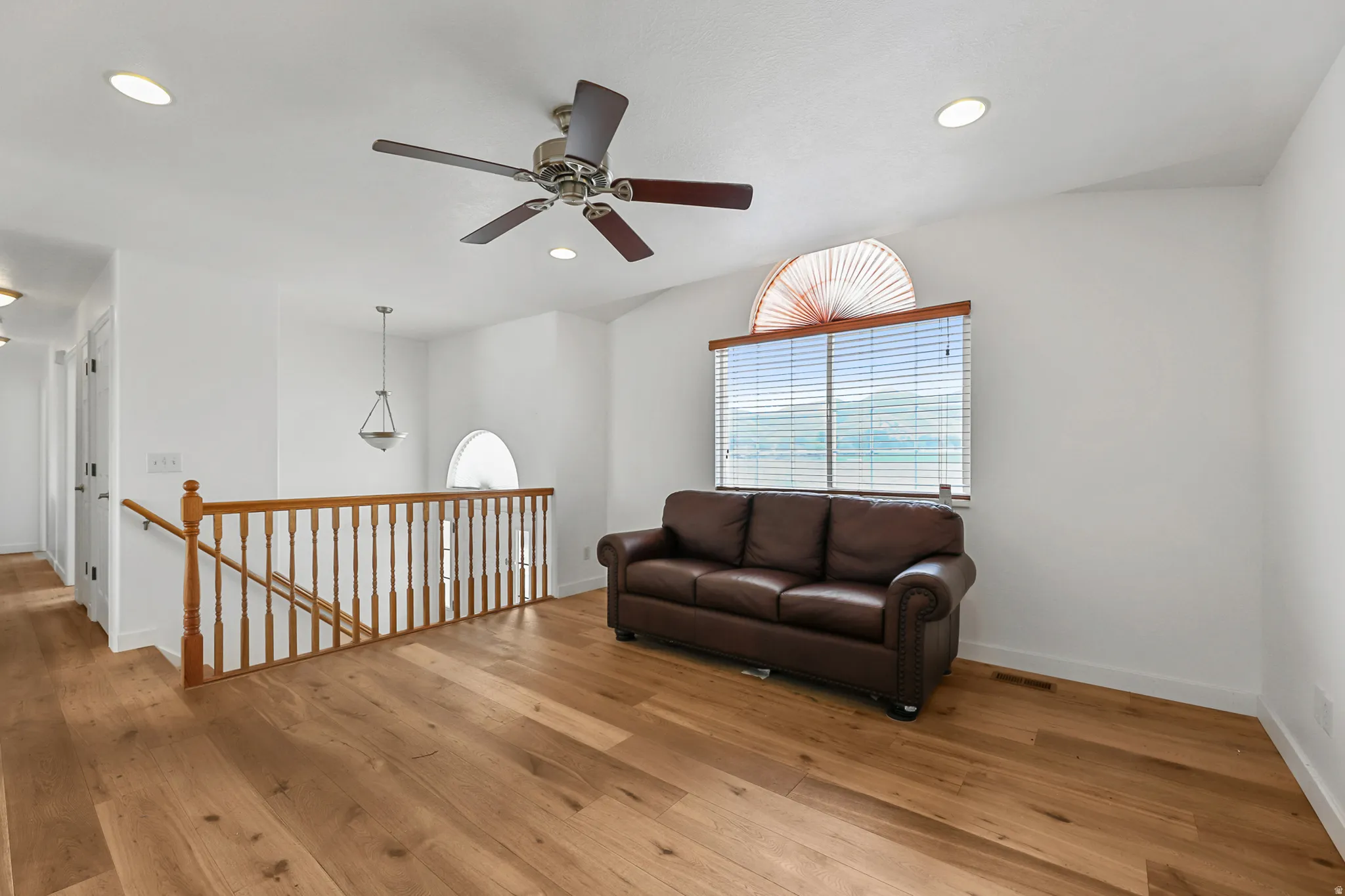 Upper-level landing featuring wood-finish flooring, a ceiling fan with light, recessed lighting, and a window with a semicircular transom above