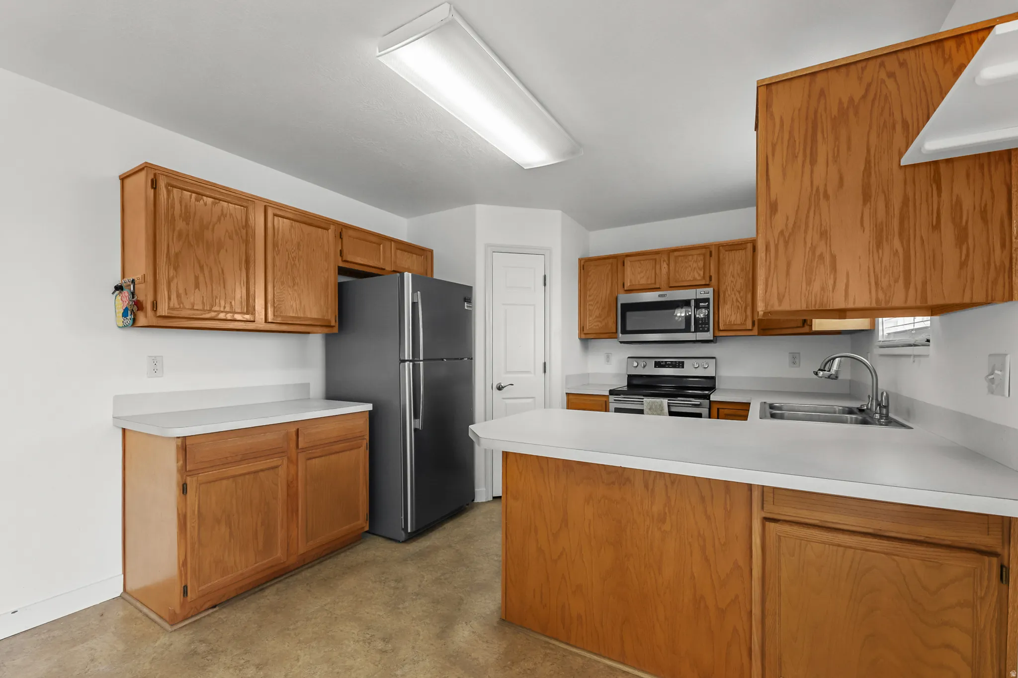 Kitchen featuring wood-finish cabinetry, light countertops, stainless steel appliances, and a peninsula with a breakfast bar
