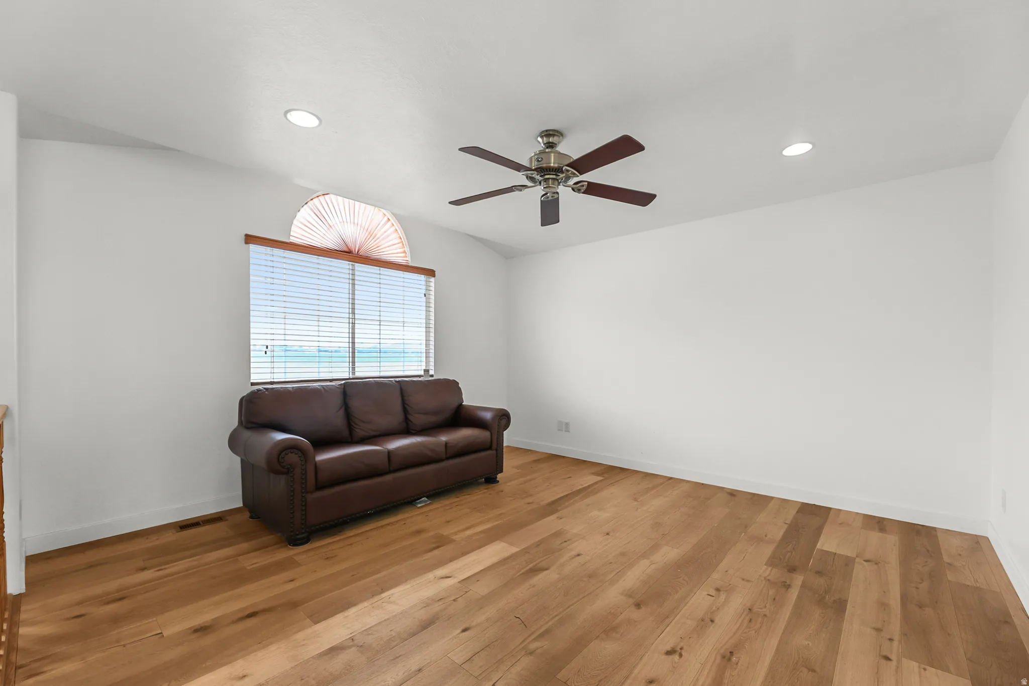 Spacious room featuring wood-finish flooring, a vaulted ceiling, recessed lighting, and a ceiling fan