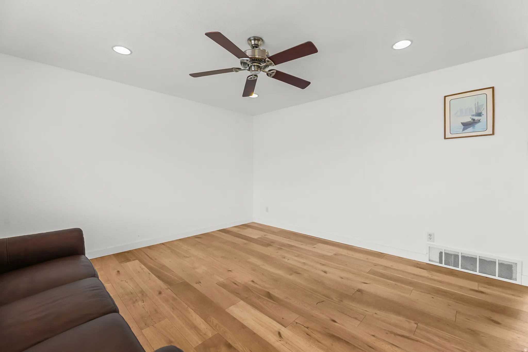 Spacious room featuring wood-finish flooring, recessed lighting, and a ceiling fan with integrated lighting