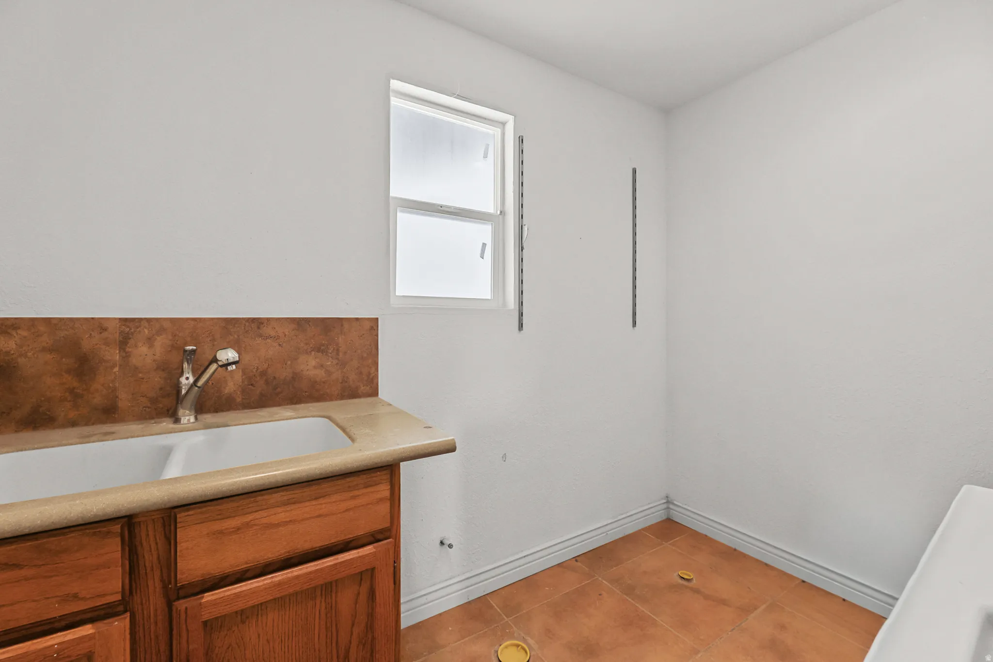 Utility room featuring a double basin sink with a chrome faucet, wood cabinetry, and a light-colored countertop