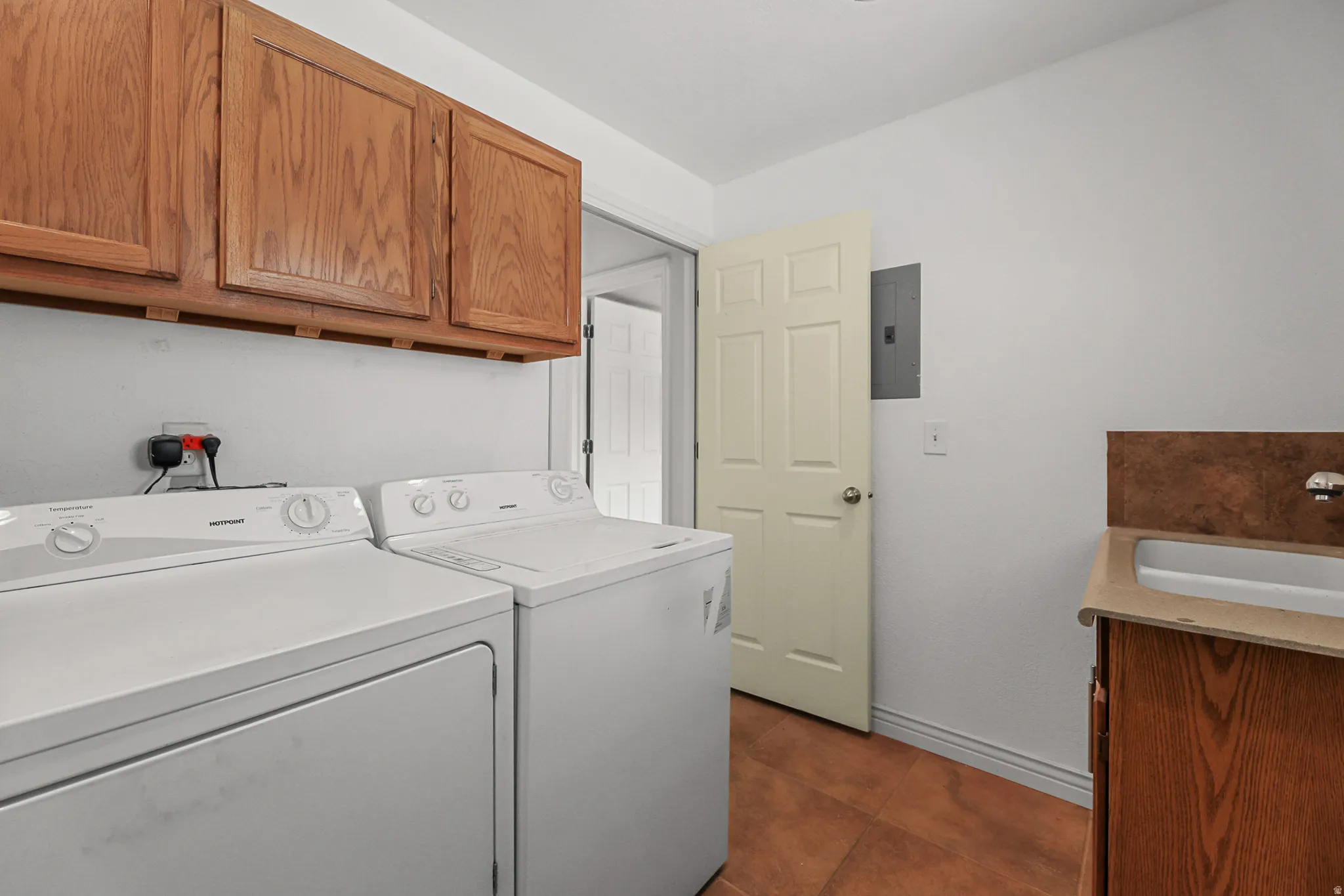 Laundry area featuring wood-finish cabinetry, a utility sink, and durable tile flooring