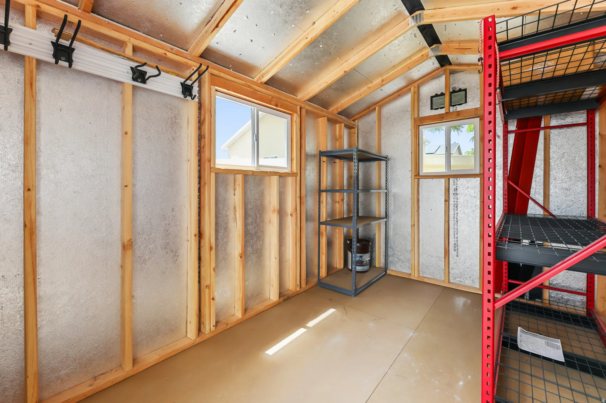 Utility shed interior featuring exposed wood framing, reflective insulation, and two windows