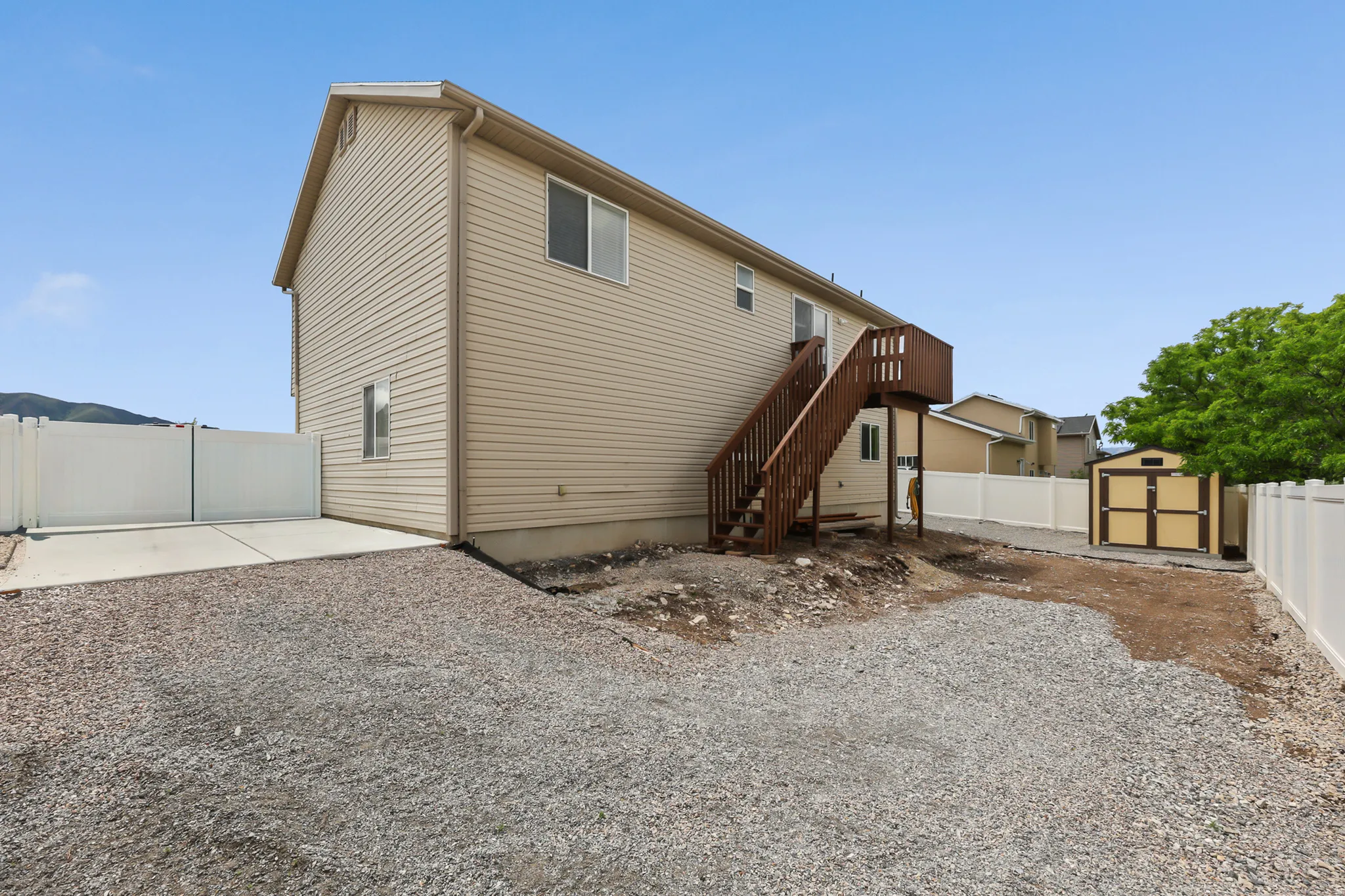 Rear exterior with beige siding, a brown wooden staircase, and a detached storage shed