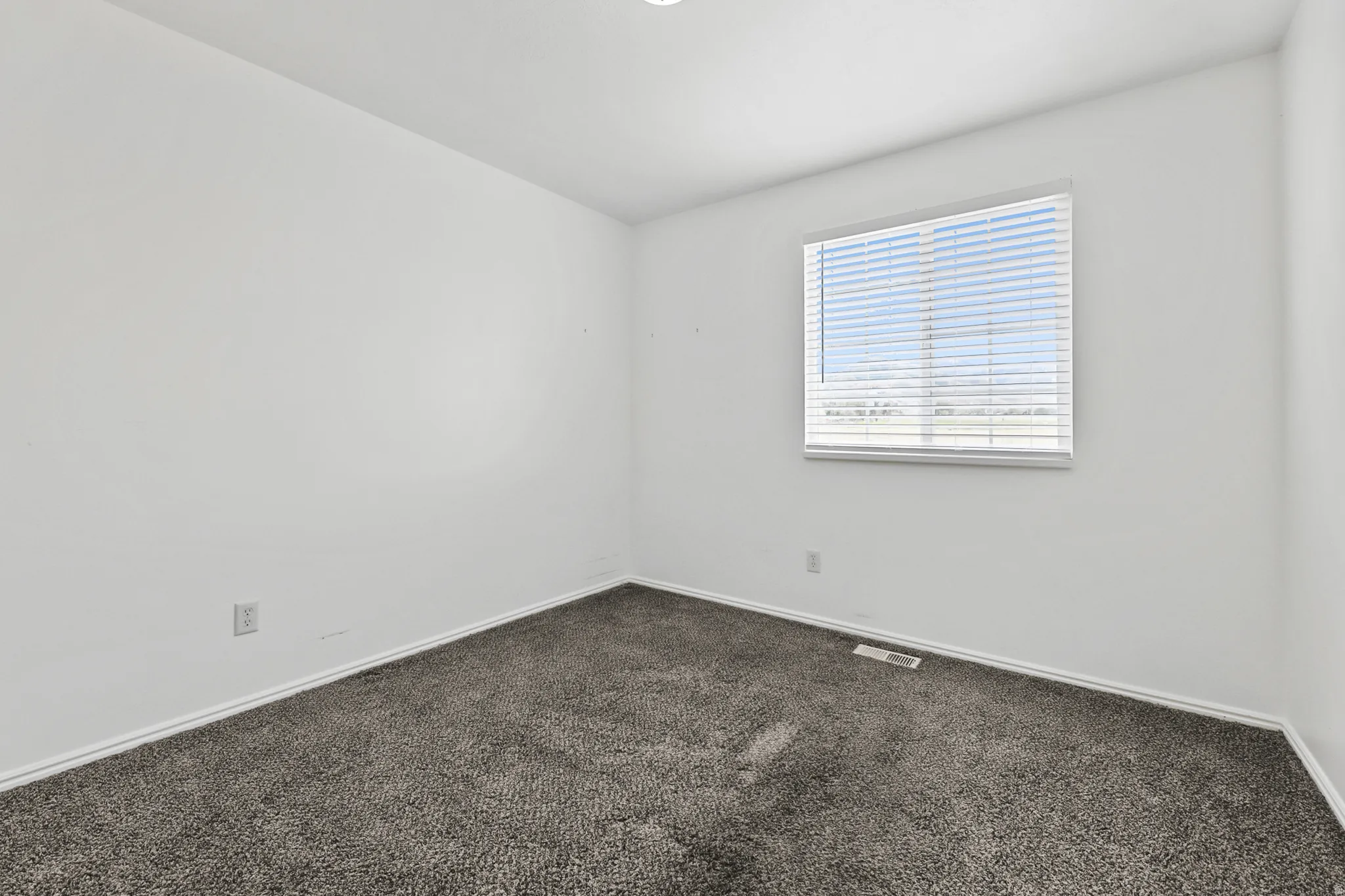 Bright room featuring a window with horizontal blinds, neutral wall paint, and gray carpet flooring