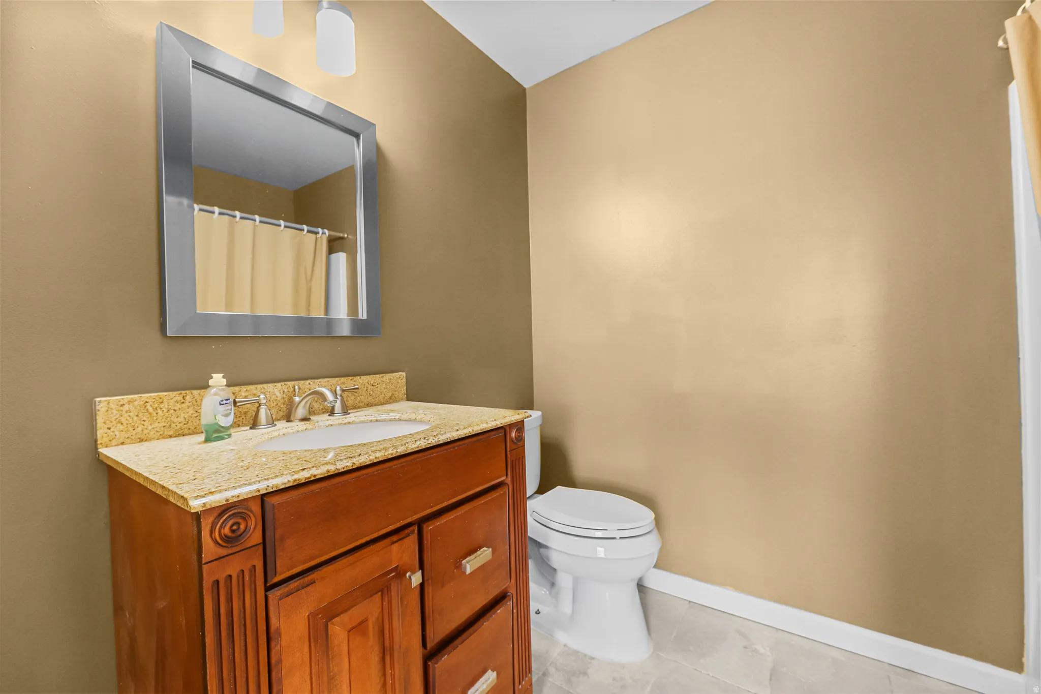 Bathroom featuring a wood-finish vanity with a light-colored countertop, an undermount sink, and a framed mirror