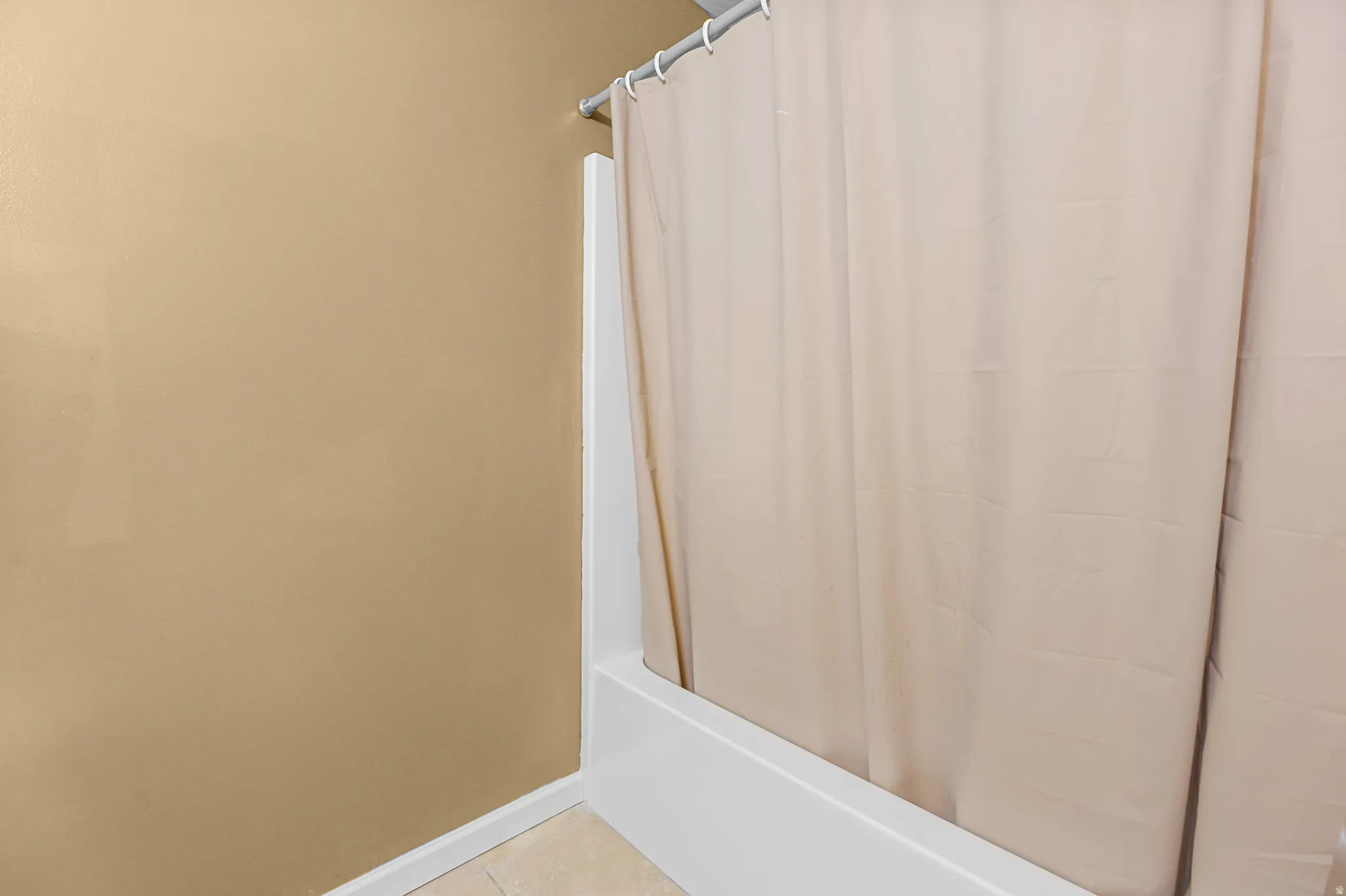 Shower/tub combination with a light-colored shower curtain, white trim, and a neutral wall color