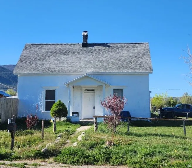 White stucco exterior featuring a gabled roof with gray shingles, a prominent front porch with white columns, and a stone chimney