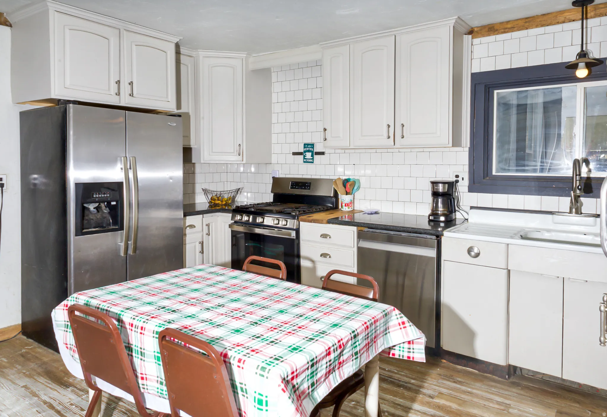 Kitchen featuring wood-finish flooring, white cabinetry, a white subway tile backsplash, and dark countertops