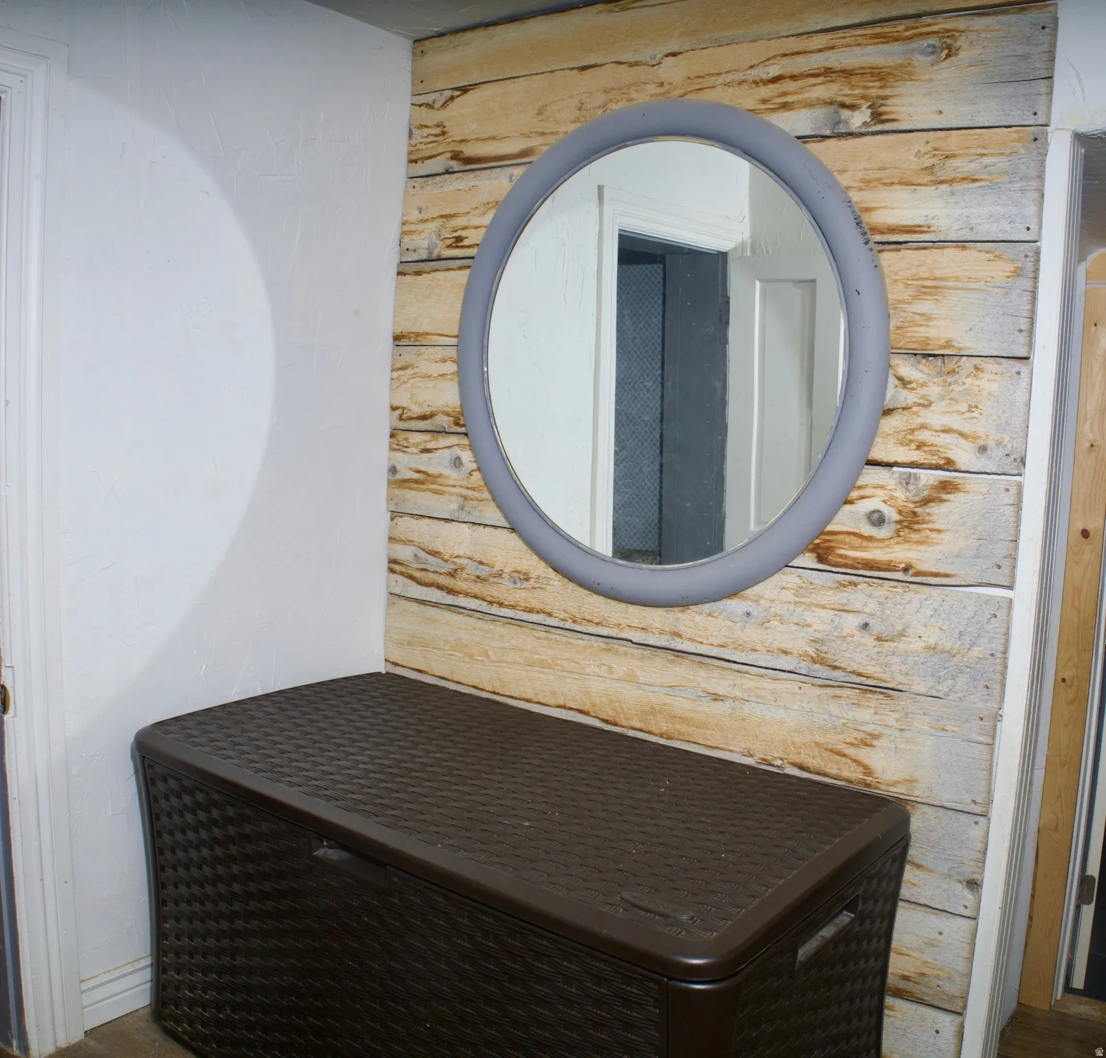 Accent wall featuring light-toned wood planks, complemented by a round mirror with a gray frame