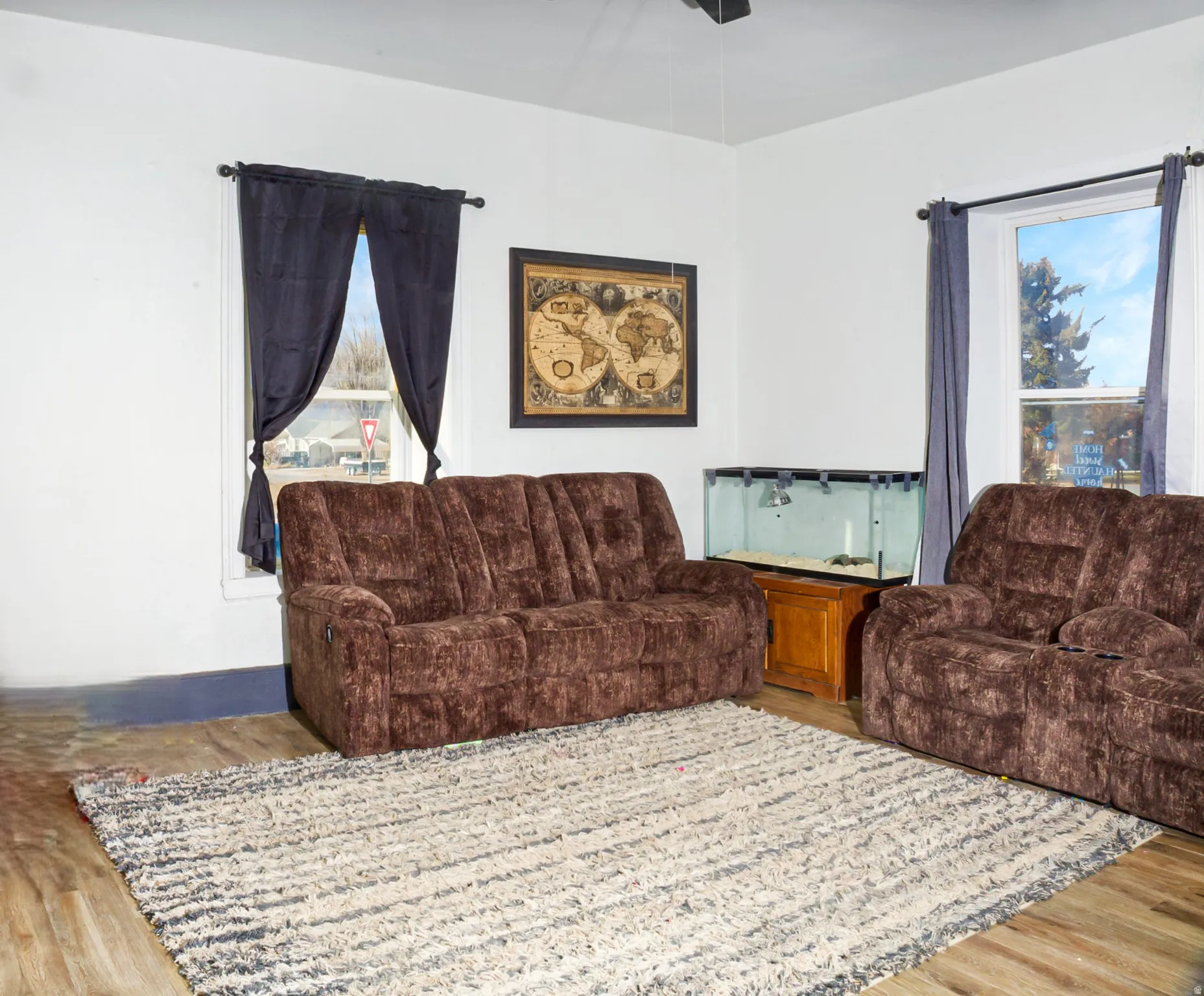 Living area featuring light wood-finish flooring, white walls, and multiple windows with dark curtains