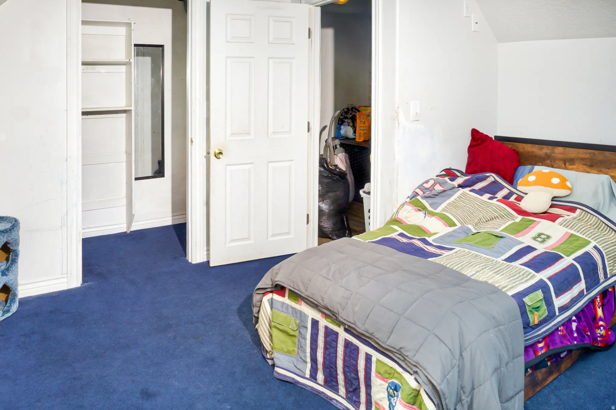 Bedroom featuring blue carpet flooring, a wood-finish headboard, white interior door, and a built-in closet with shelving and a mirror