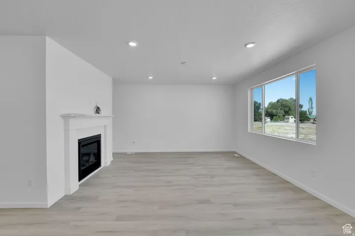 Spacious living area featuring a built-in fireplace with a white mantel, light wood-finish flooring, recessed lighting, and a large multi-pane window