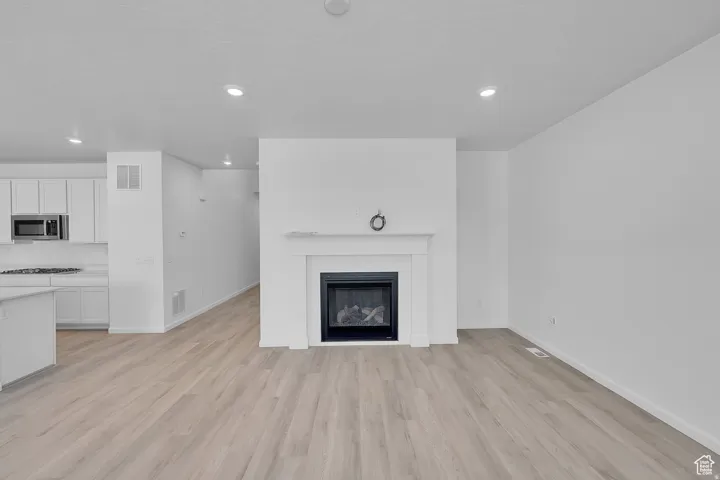 Living area featuring a central fireplace with a white mantel, wood-finish flooring, recessed lighting, and a neutral color palette