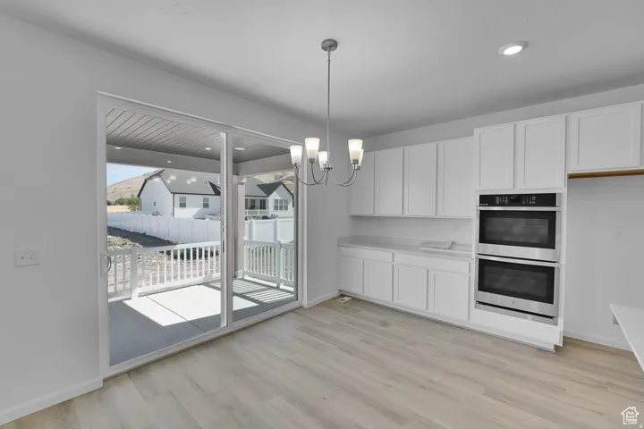 Modern kitchen with light wood-finish flooring, white cabinetry, and stainless steel double ovens