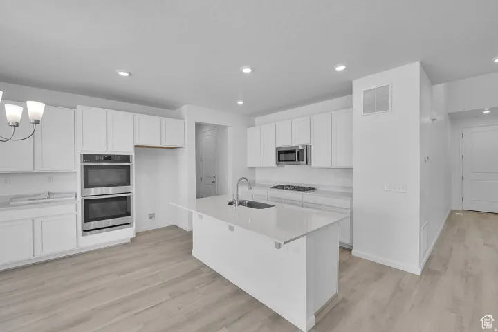 Contemporary kitchen featuring white cabinetry, light-toned wood-finish flooring, recessed lighting, and a kitchen island with an integrated sink
