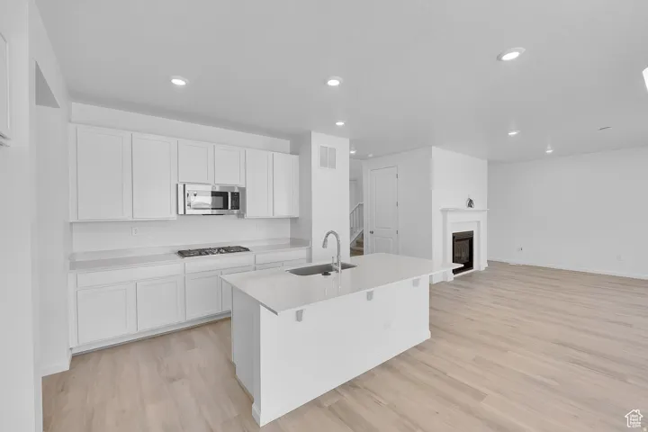 Open-concept kitchen and living area featuring a central island with an integrated sink, white cabinetry, a built-in microwave, and a gas range