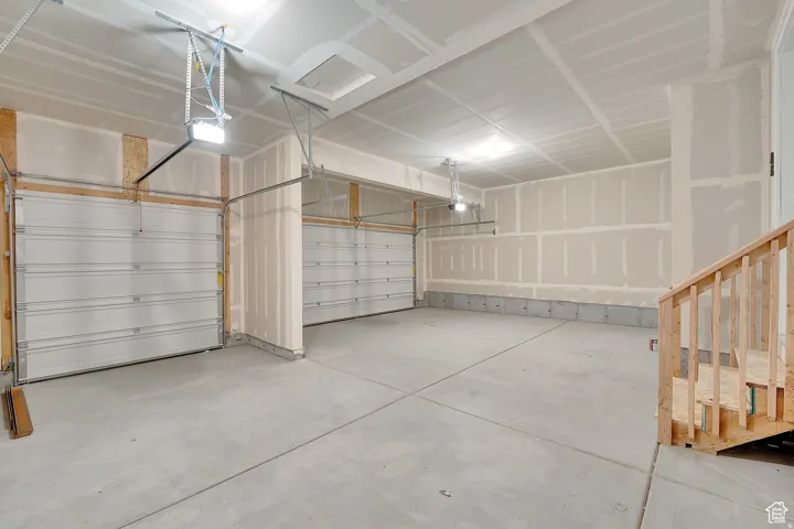 Spacious multi-car garage with concrete flooring, two overhead garage doors, and a partial wood staircase