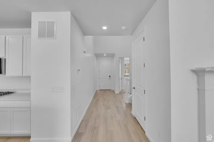 Bright hallway featuring light wood-finish flooring, recessed lighting, and a white paneled door